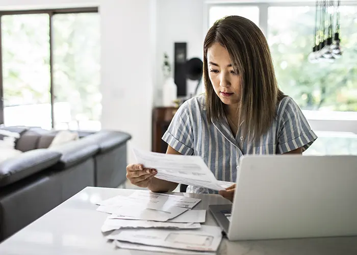 Woman sitting in front of a laptop, sorting through paperwork