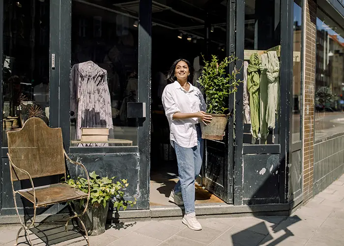 Female small business owner walking out of shop holding a potted plant